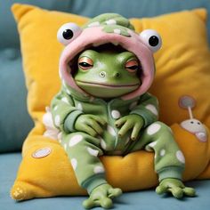 a stuffed frog sitting on top of a yellow pillow next to a green pillow with polka dots