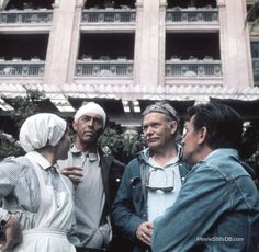 three men and two women standing in front of an apartment building talking to each other