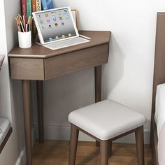 a laptop computer sitting on top of a wooden desk next to a white chair and bed