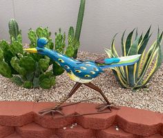 a blue bird statue sitting on top of a red brick wall next to green plants