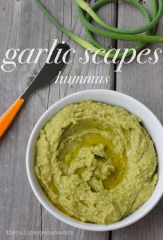 a white bowl filled with green hummus next to an orange fork and carrots