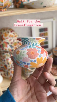 a hand holding a colorful vase in front of a shelf with plates and bowls on it