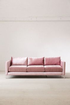 a pink couch sitting on top of a wooden floor next to a white wall in an empty room