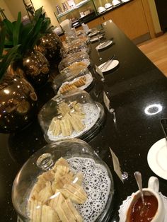 plates and bowls filled with food sitting on a black counter top next to vases