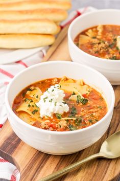 two bowls of soup on a wooden cutting board with bread in the backgroud