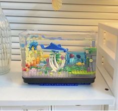 a fish tank filled with colorful legos on top of a white table next to a vase