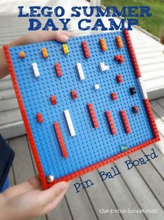 a person holding up a lego summer day camp pin ball board with blocks and balls on it