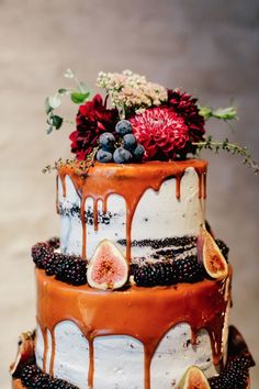 a three tiered cake with fresh fruit and flowers on top, dripping in chocolate