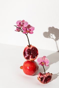 two pomegranates with one cut open and the other half opened, sitting on a white surface