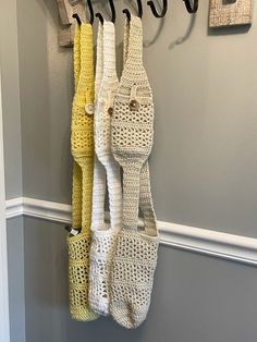 three crocheted purses hanging from hooks on the wall in front of a gray wall