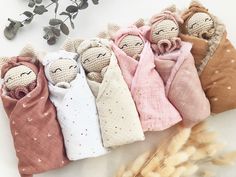 five cloth dolls are wrapped in blankets on a white surface next to some dried flowers