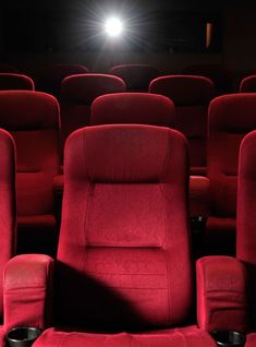 rows of red chairs in front of a projector screen with light shining on them