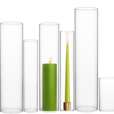 a green candle is surrounded by tall glass vases and candlesticks on a white background