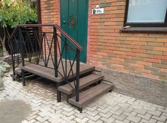 a set of stairs next to a green door on a brick building with steps leading up to it