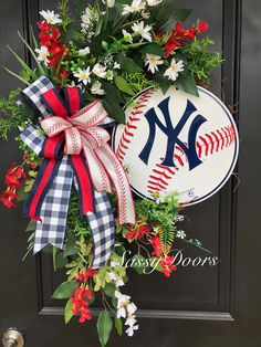 a new york yankees baseball wreath on a door with red flowers and greenery next to it