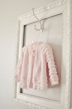 a white frame holding a pink sweater hanging on the wall