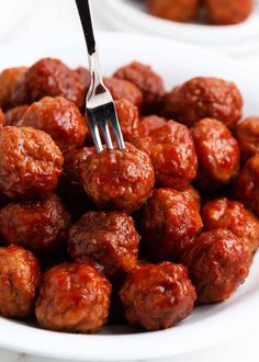 a fork is stuck into some meatballs on a white plate with another dish in the background