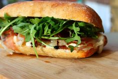 a close up of a sandwich on a cutting board with arugula and cheese