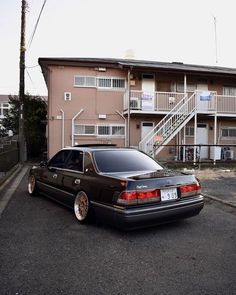 a black car parked in front of an apartment building with stairs leading up to the second floor