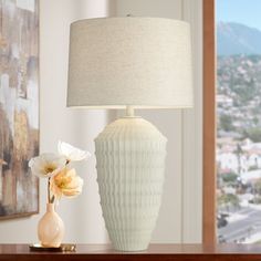 a white vase sitting on top of a wooden table next to a lampshade