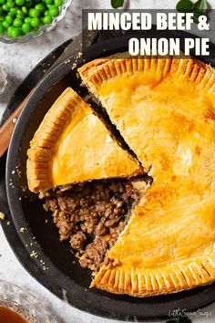 a minced beef and onion pie on a black plate with one slice cut out