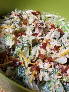 a green bowl filled with broccoli, cheese and other toppings on top of a table