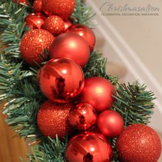 red christmas ornaments are hanging on a green garland with pine needles and glittered balls