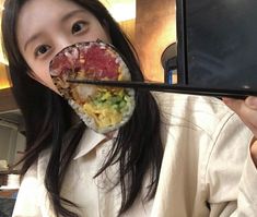 a woman holding up a sushi with chopsticks to her face