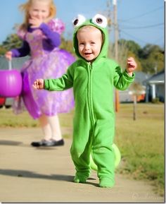 a young child in a frog costume walking down a sidewalk with another person behind him