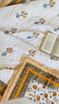 an open book sitting on top of a bed next to two pillows and a blanket