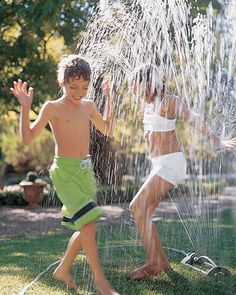 two young boys playing in the sprinkle from a water hose that is spraying them with their hands