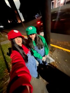 two young women sitting on the side of a road at night wearing green and red hats