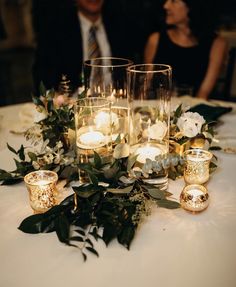 a table with candles, flowers and greenery is set up for a wedding reception