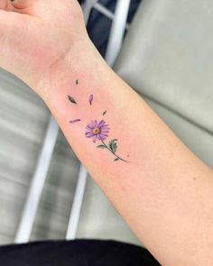 a woman's arm with a small purple flower tattoo on the left side of her arm