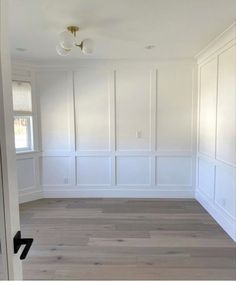 an empty room with white paneling and wood floors