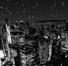 black and white cityscape at night with snow falling from the sky over skyscrapers