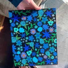 a person holding up a piece of paper with blue and green flowers painted on it