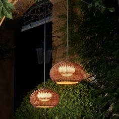 two lights hanging from the side of a building in front of some bushes and trees