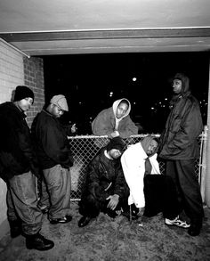 four men are standing in front of a chain link fence and one man is bending over