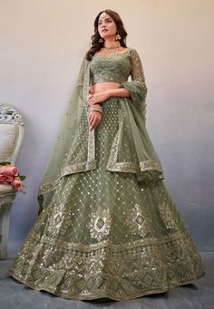 a woman in a green lehenga standing next to a white vase with flowers