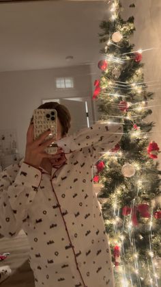 a woman taking a selfie in front of a christmas tree with her cell phone