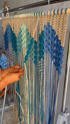 a woman is working on an art project with blue and green yarn hanging from the ceiling