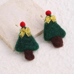 two small christmas trees with bows on them are sitting next to a stone block and snow