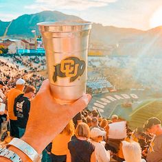 a person holding up a cup in front of a crowd at a football game with mountains in the background