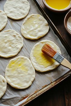 homemade flatbreads being prepared on a baking sheet with a brush and bowl of oil