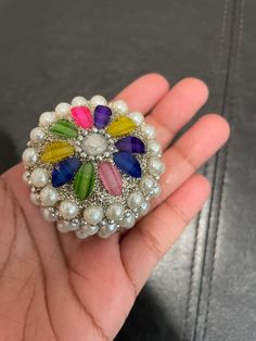 a hand holding a colorful brooch with pearls