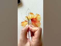 a person is holding a paintbrush and painting a flower