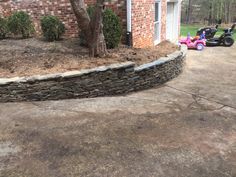 a large stone wall in front of a house with a lawn mower parked next to it