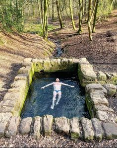 a woman swimming in a small pool surrounded by rocks and trees, with her arms spread out