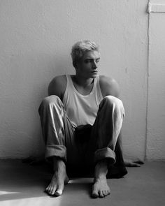 a young man sitting on the floor in front of a wall